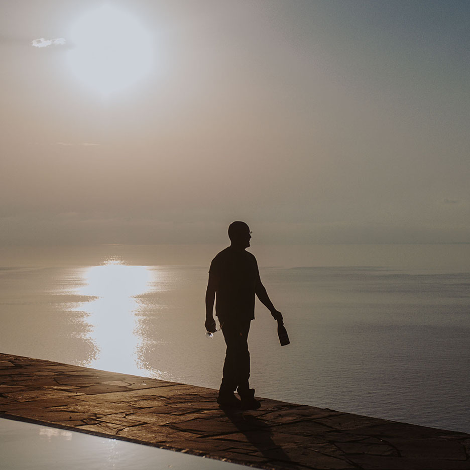 Silhouette d'un homme avec une bouteille et un verre de vin au coucher du soleil sur la mer.