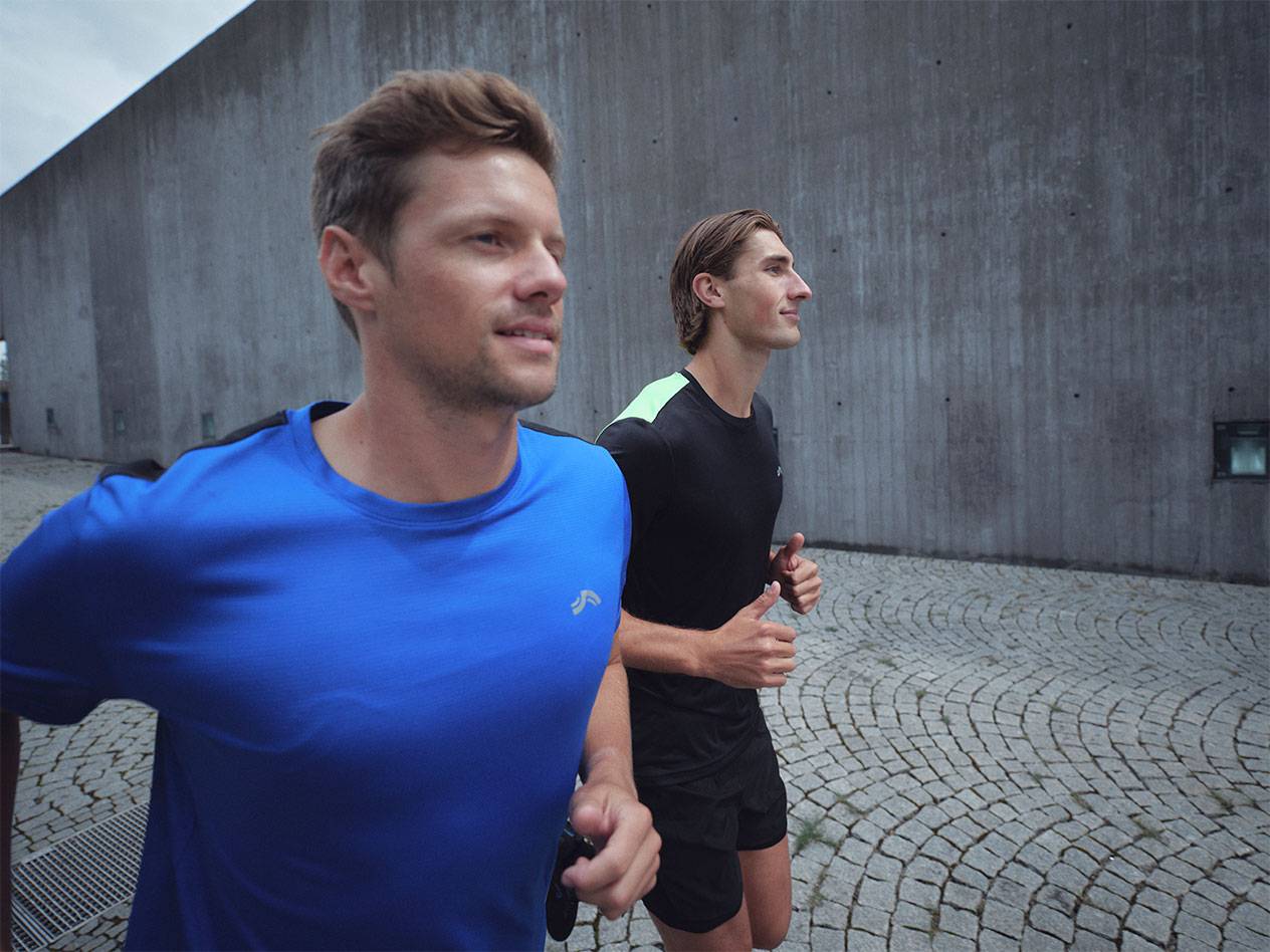 Deux hommes courent en t-shirts et shorts de sport, un bleu et un noir.