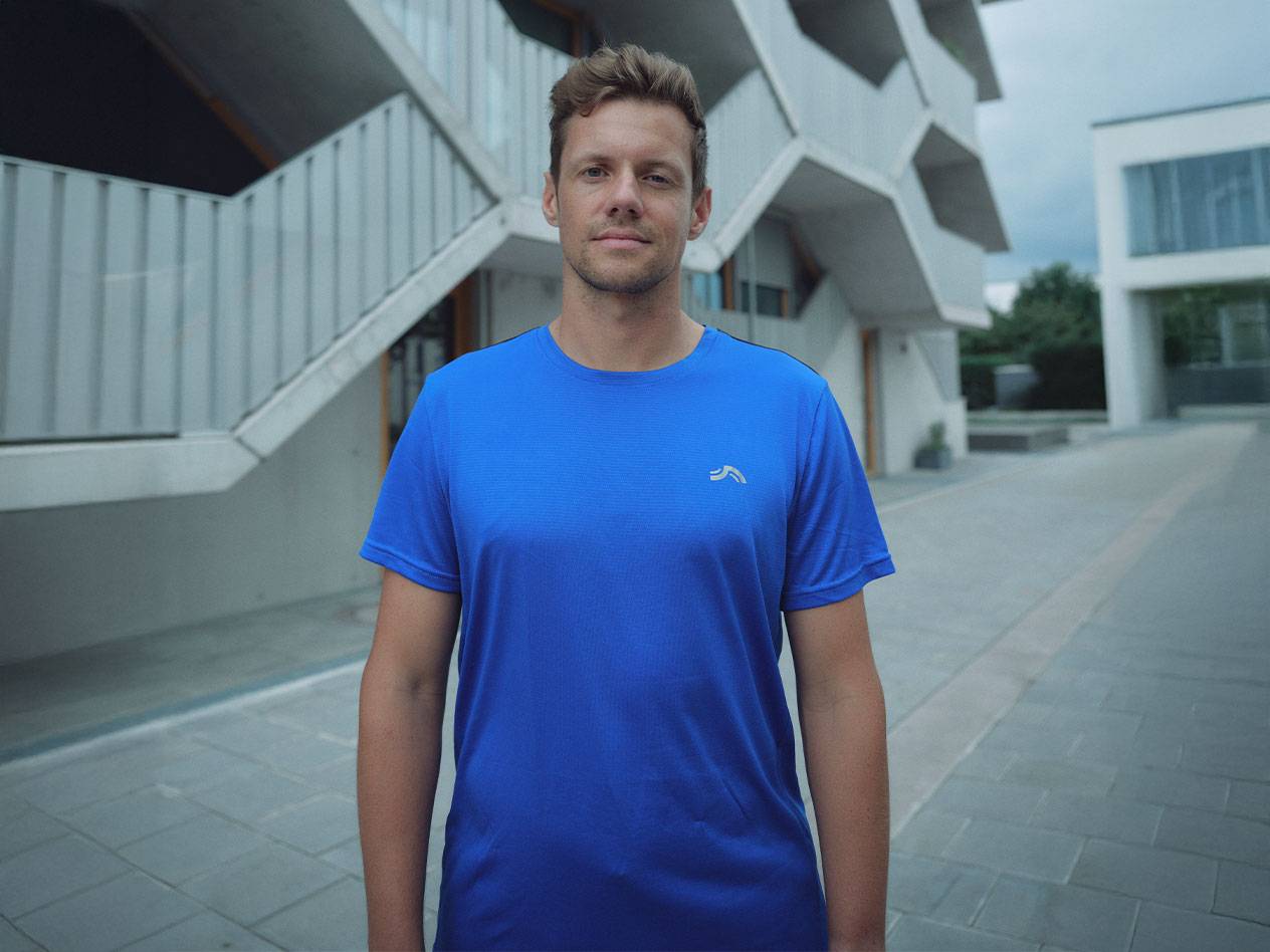 Homme en t-shirt de sport Crivit bleu, avec un bâtiment moderne en arrière-plan.