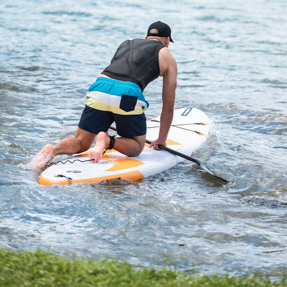 Homme à genoux sur une planche de paddleboard avec pagaie dans l'eau.