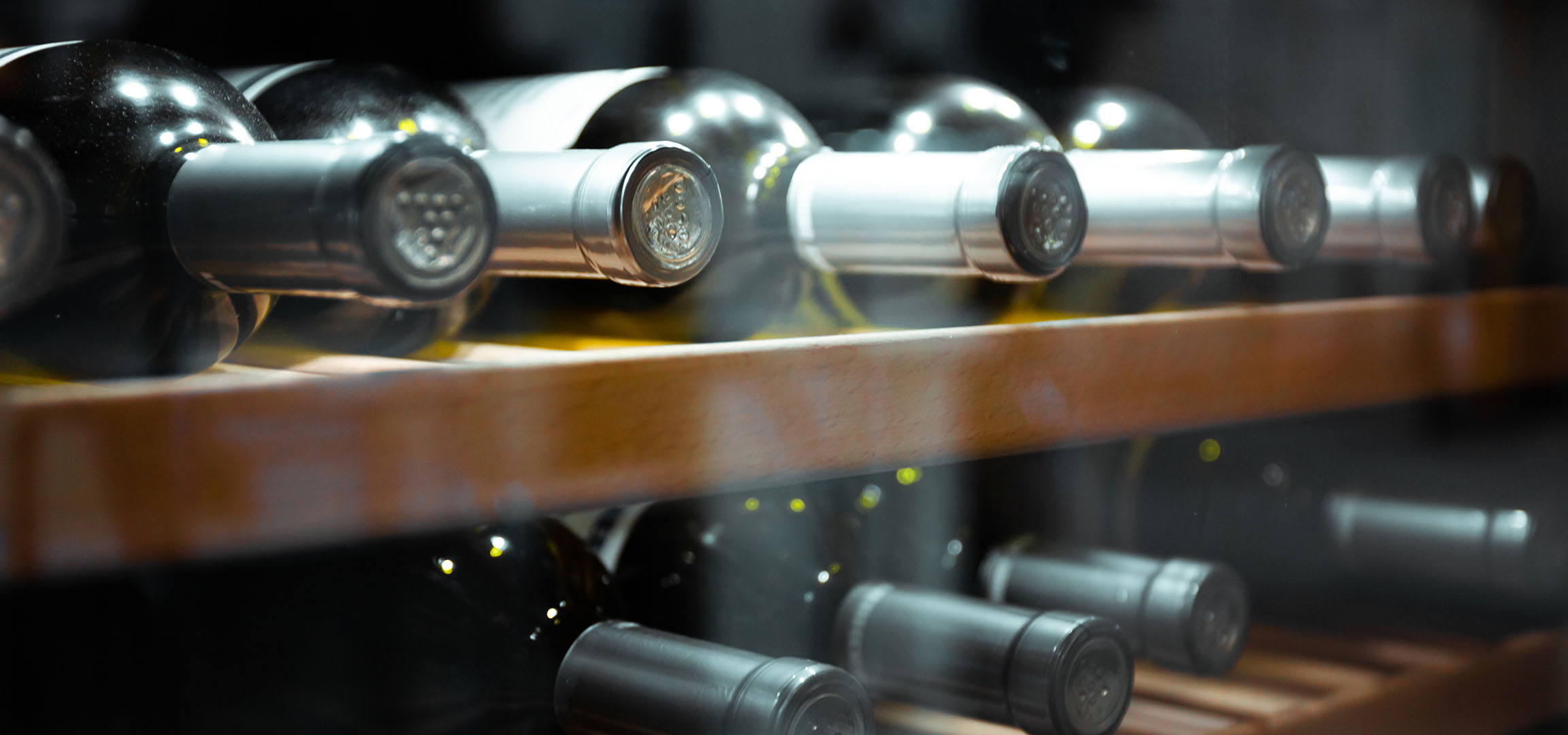 Gros plan de bouteilles de vin sur une étagère en bois, montrant leurs capsules et reflets.