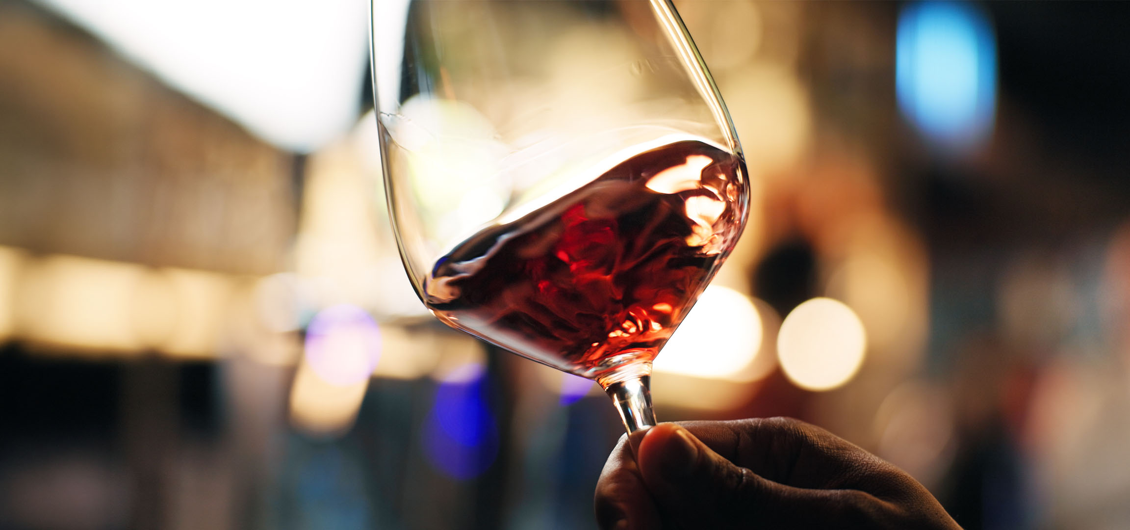 Gros plan d'un verre de vin rouge avec des lumières floues en arrière-plan.