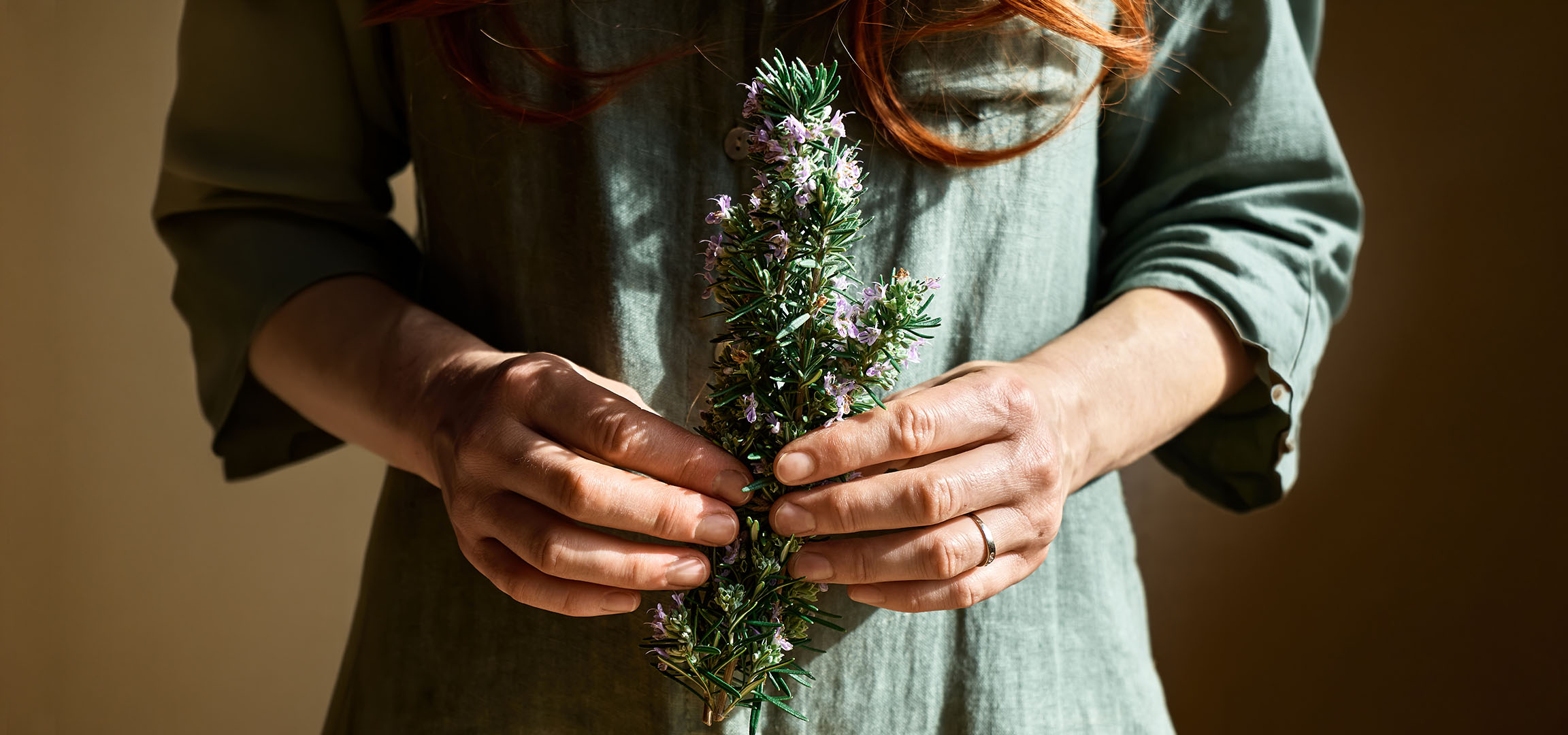 Femme en robe verte tenant un bouquet de romarin en fleurs.