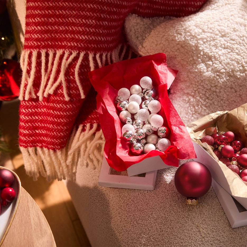 Décorations de Noël: boules rouges et argentées dans des boîtes, avec une couverture et un coussin.