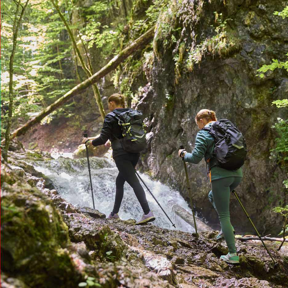 Deux femmes avec des sacs à dos et des bâtons de trekking marchent le long d'une cascade.