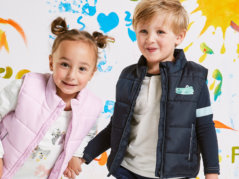 Deux jeunes enfants souriants portent des vestes matelassées colorées.