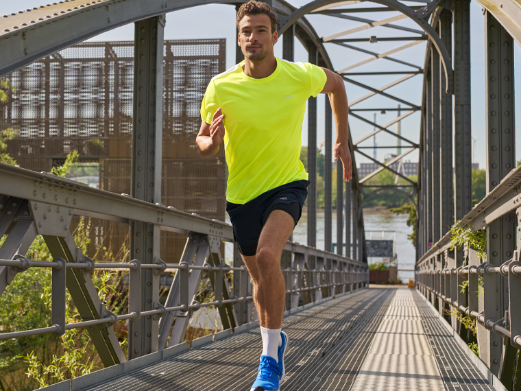 Un homme court sur un pont en portant un t-shirt jaune vif et un short de sport.