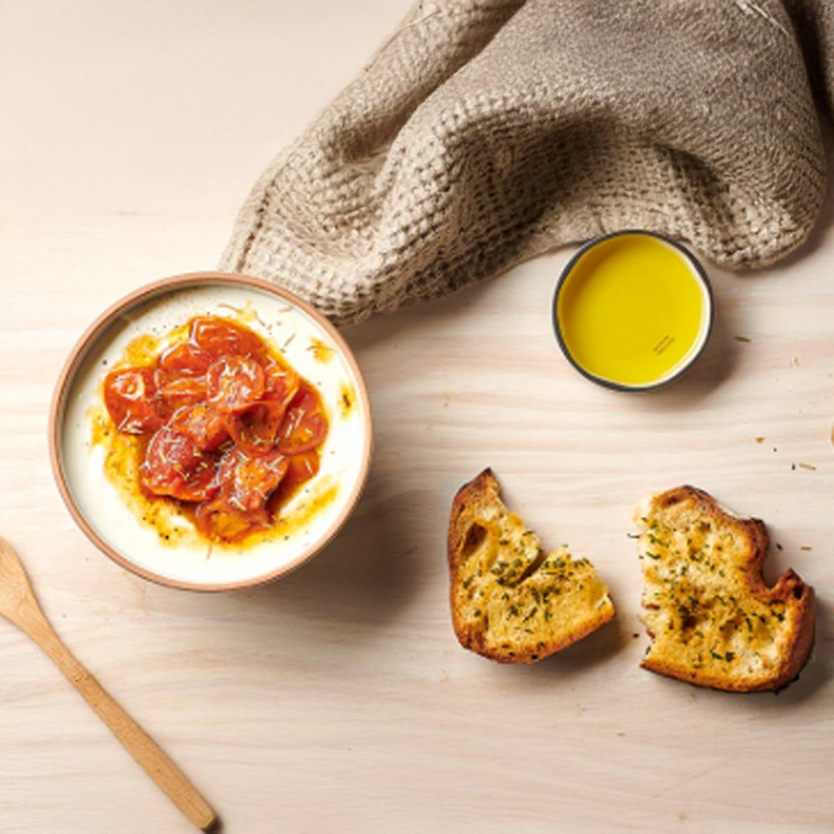 Un bol de yaourt au miel et tomates rôties, accompagné de pain grillé et d'huile d'olive.