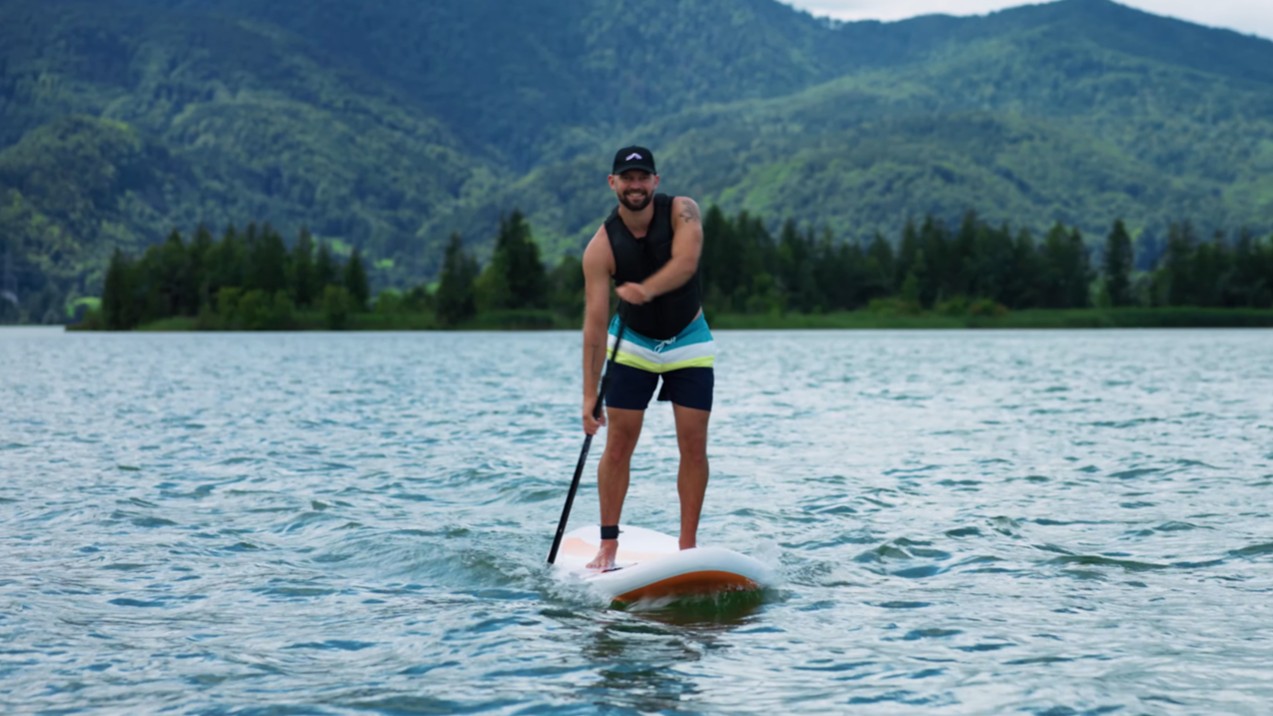 Homme sur paddleboard sur un lac avec des montagnes en arrière-plan.