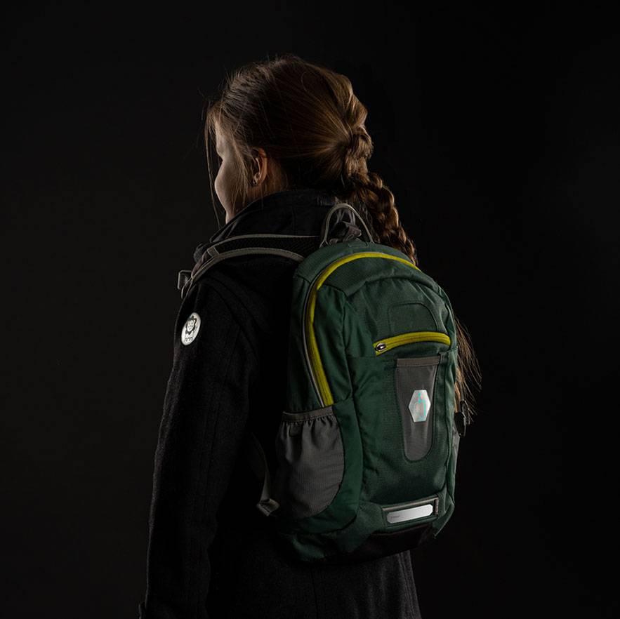 Femme avec un sac à dos vert et gris sur le dos, sur fond sombre.