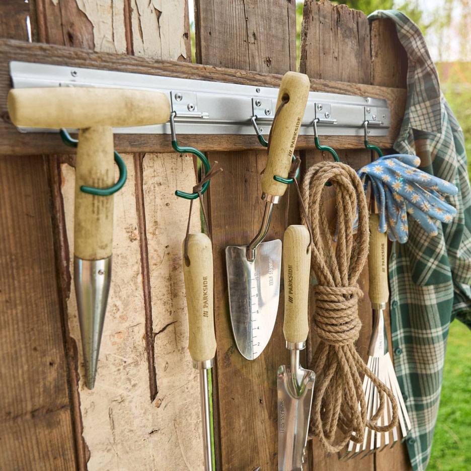 Outils de jardinage et corde suspendus à un mur en bois, à côté d'une chemise et de gants.