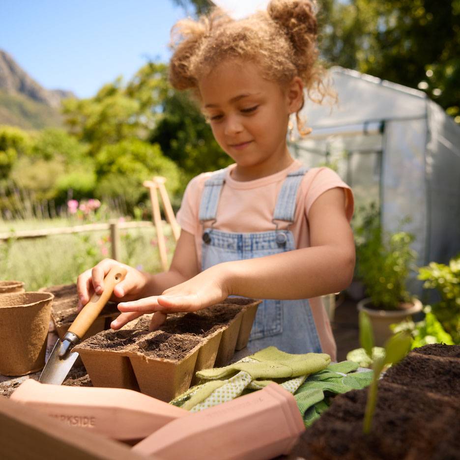 Fille plantant des graines dans des pots en tourbe avec des outils de jardinage et des gants.
