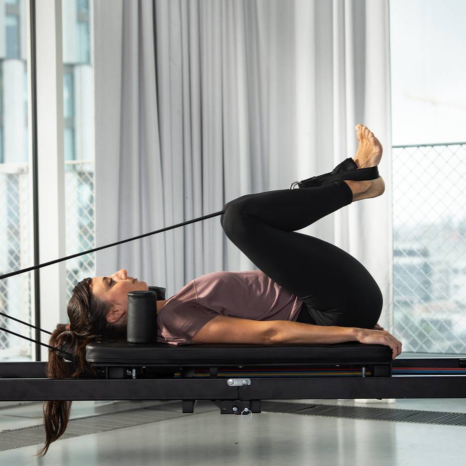 Femme faisant du Pilates sur un reformer, jambes levées.