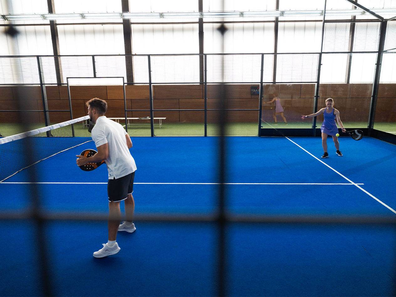 Deux personnes jouent au padel sur un court bleu, l'homme tient une raquette.