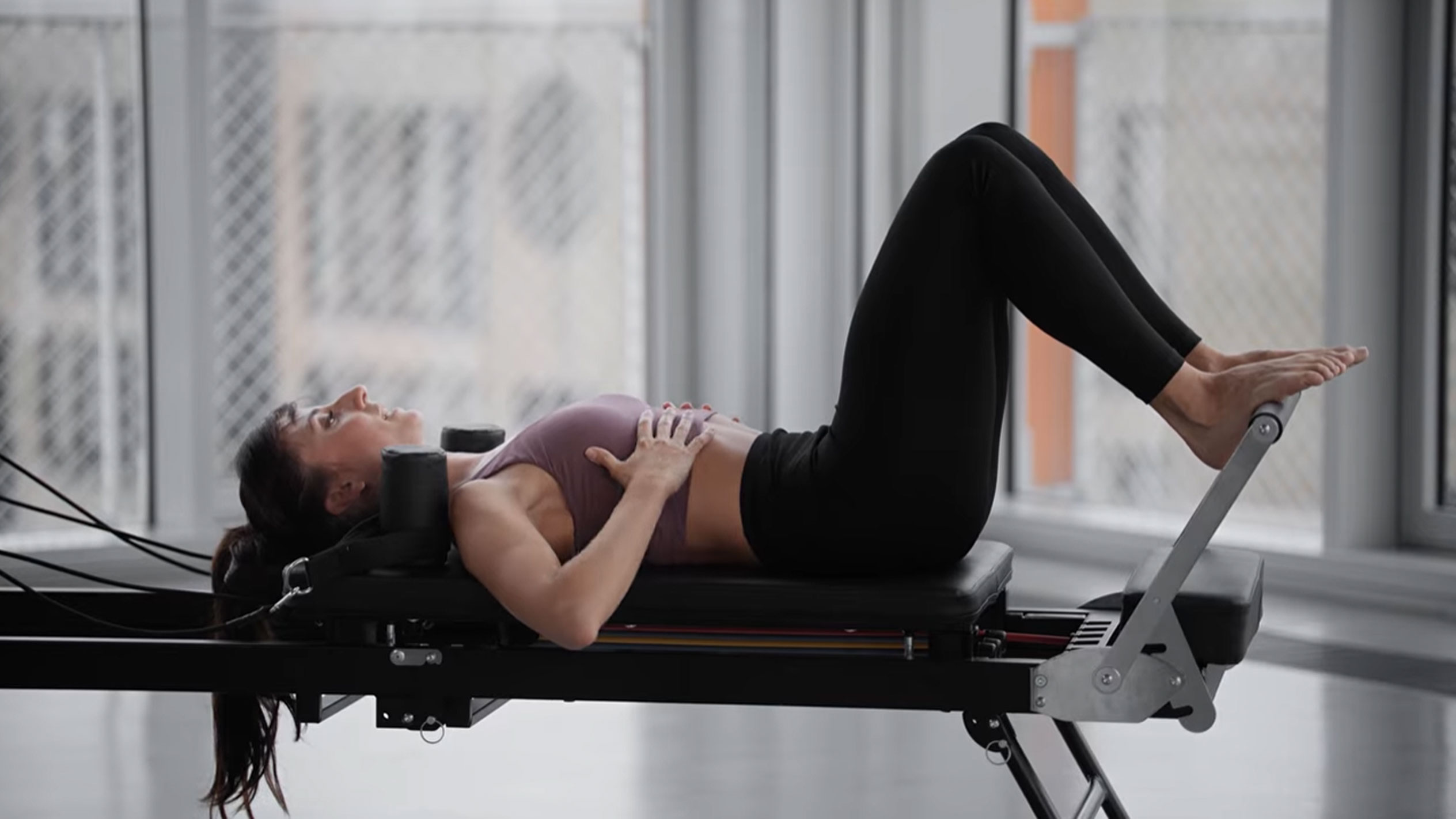 Femme faisant du Pilates sur un reformer, les mains sur la poitrine.