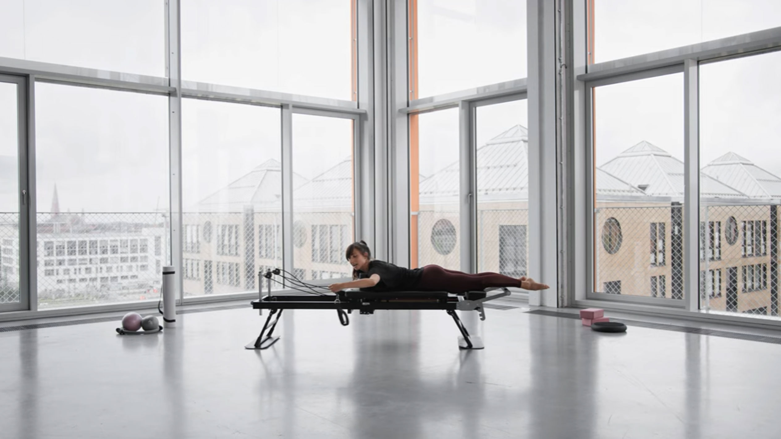 Femme faisant du Pilates sur un reformer, avec vue sur la ville.