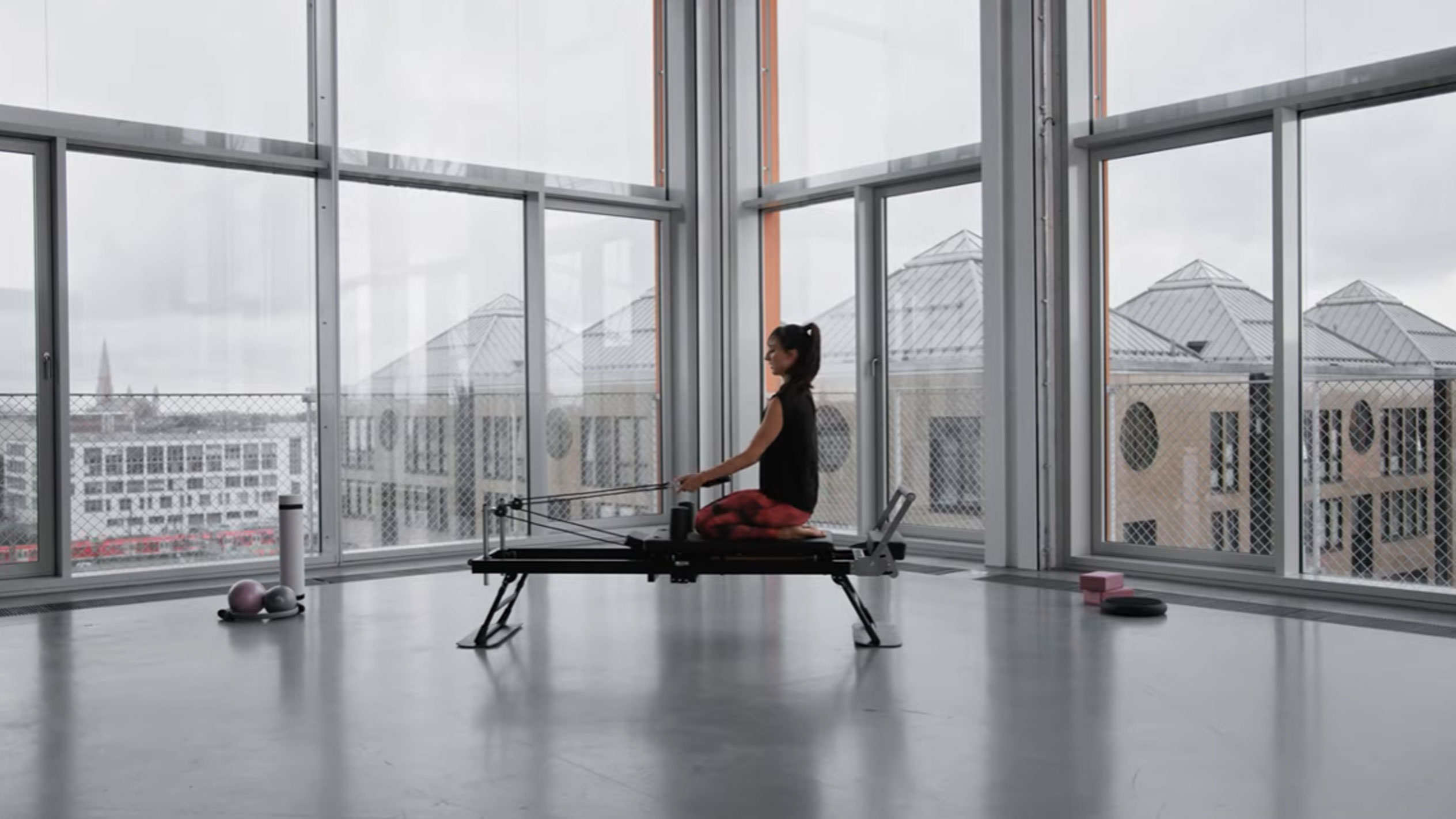 Femme faisant du Pilates sur un reformer, avec vue sur la ville.