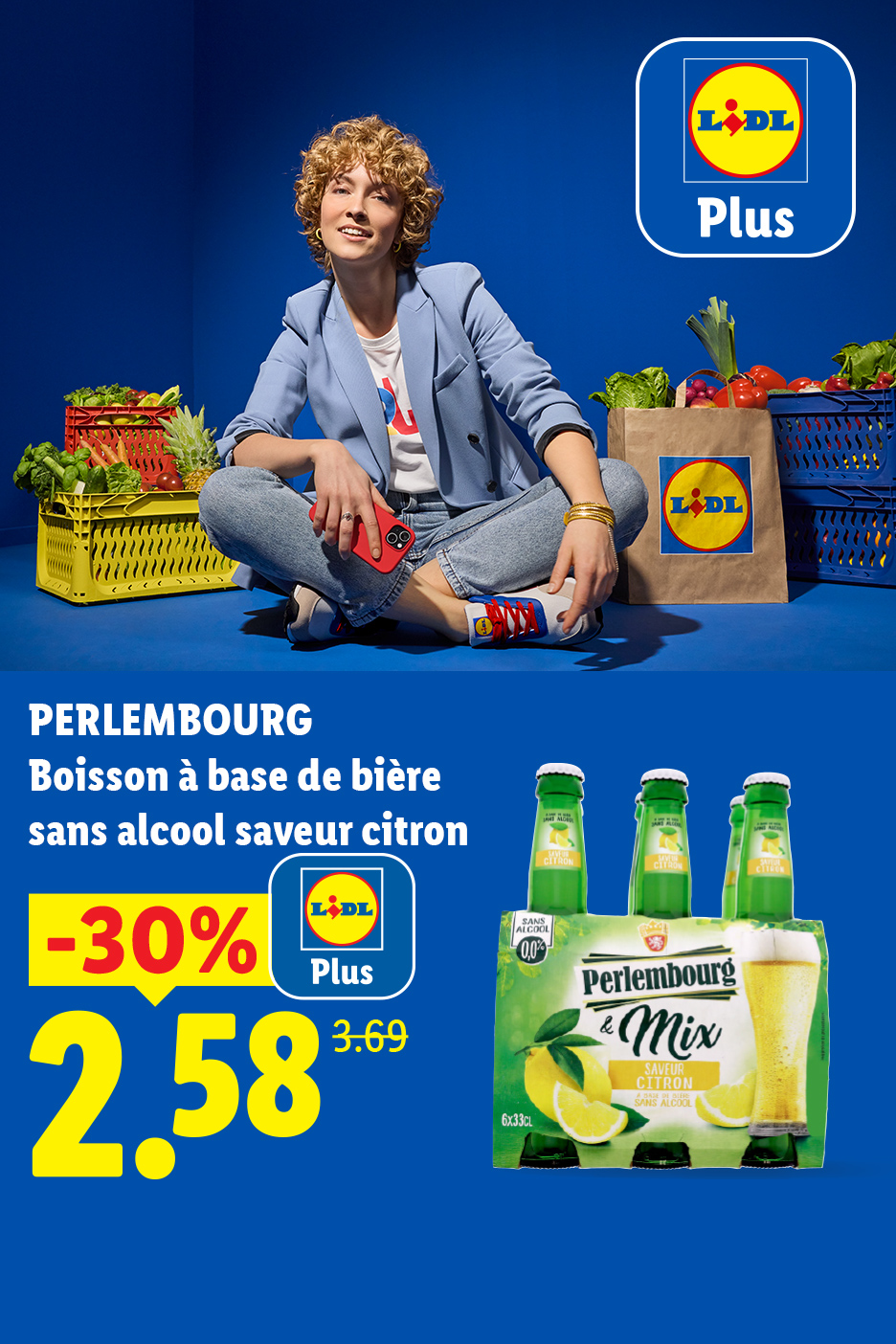 Une femme souriante assise au milieu de cagettes de fruits et légumes, avec un pack de bière sans alcool au citron en promotion.