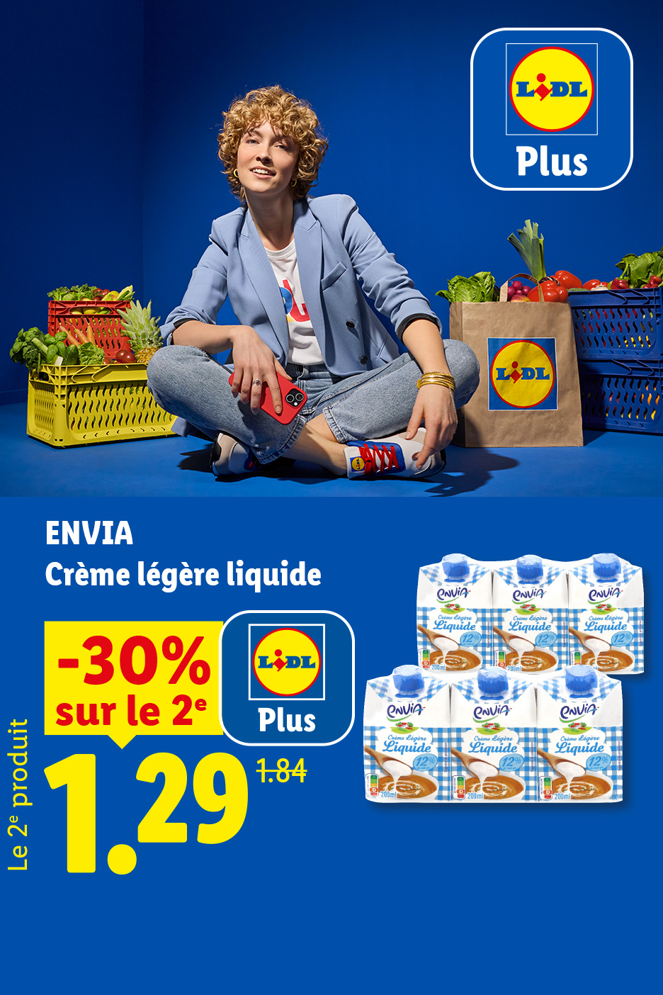 Une femme souriante assise parmi des caisses de fruits et légumes, avec une offre sur de la crème liquide.