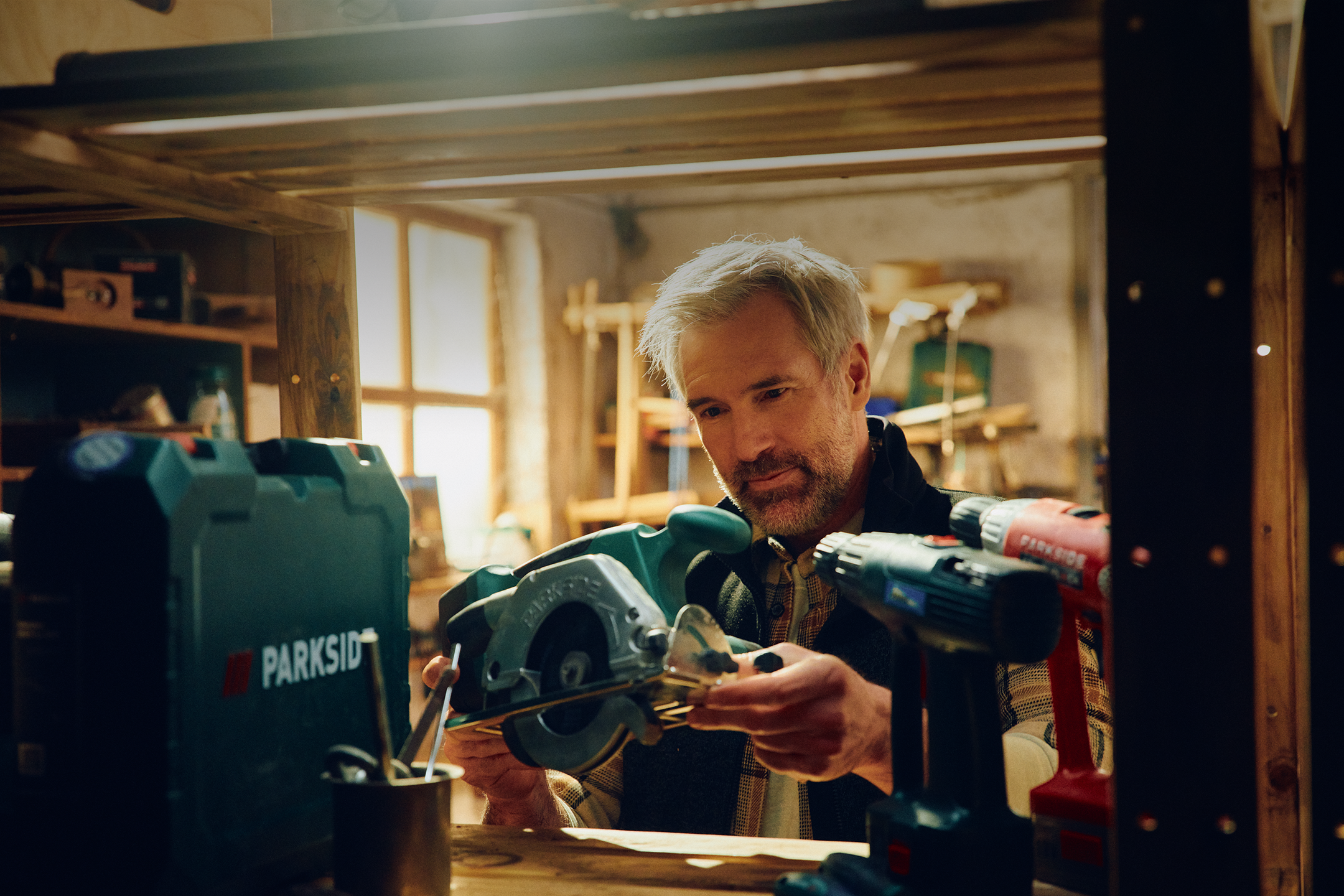 Un homme examine une scie circulaire dans un atelier, avec des outils électriques à côté.