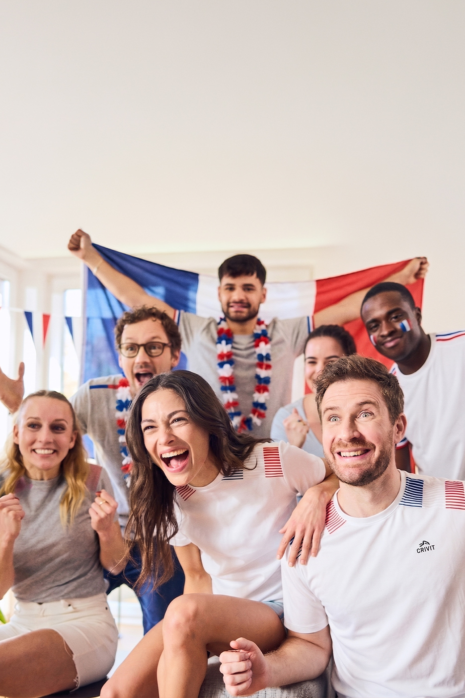 Un groupe d'amis joyeux portant des t-shirts blancs et des guirlandes aux couleurs de la France, agitant un drapeau français.
