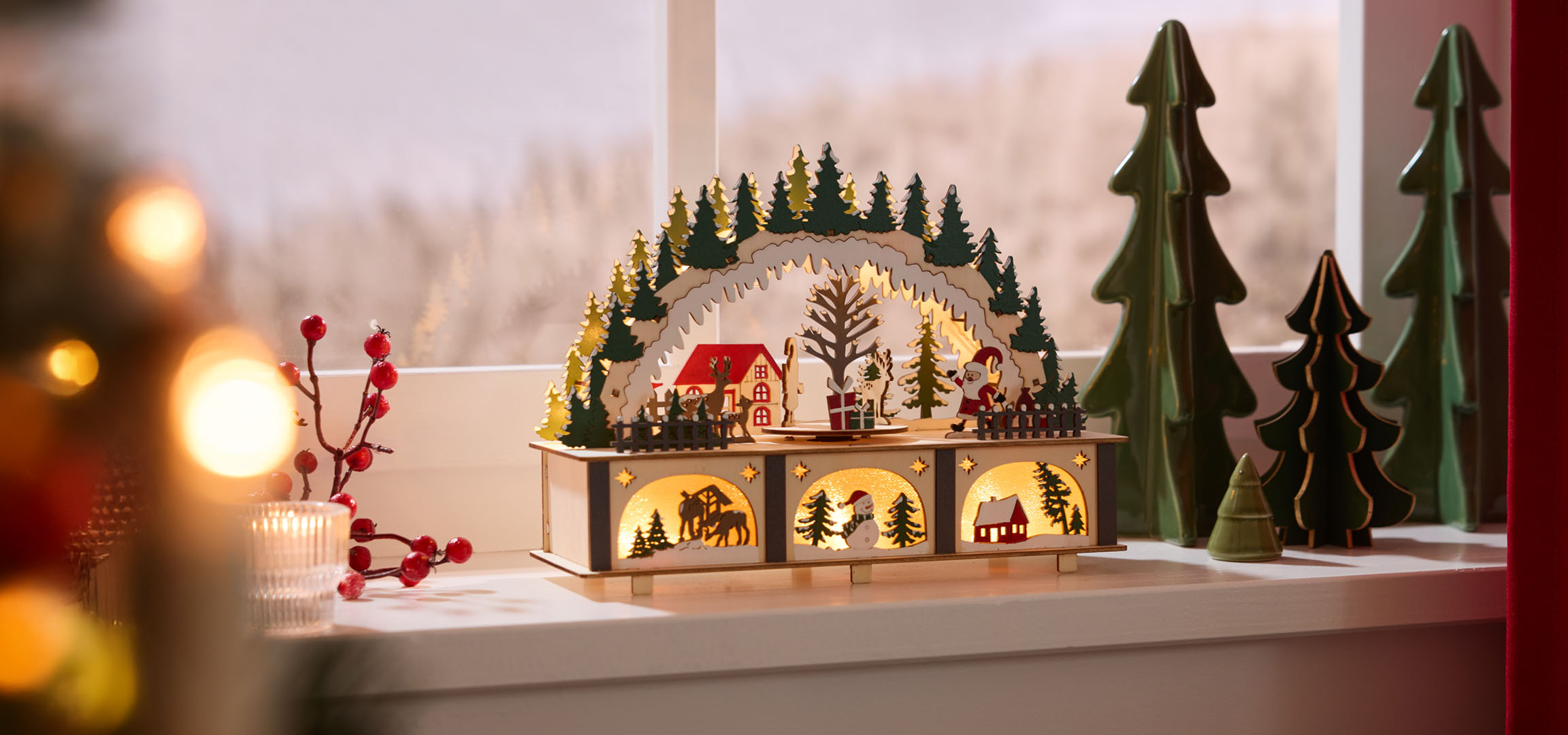 Décorations de Noël: paysage en bois illuminé avec maisons et arbres, baies rouges et bougie.