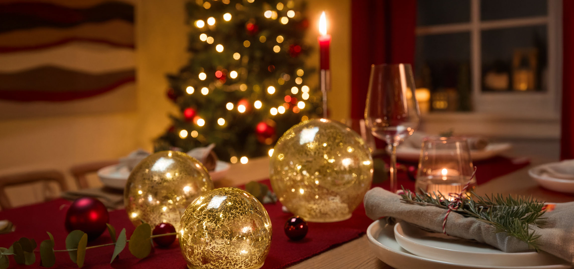 Décoration de table de Noël avec des globes lumineux dorés, des boules rouges et du sapin.