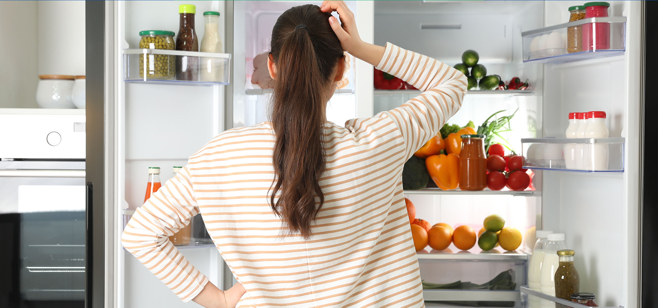 Femme regardant dans un réfrigérateur ouvert rempli de légumes frais, de fruits et de boissons.
