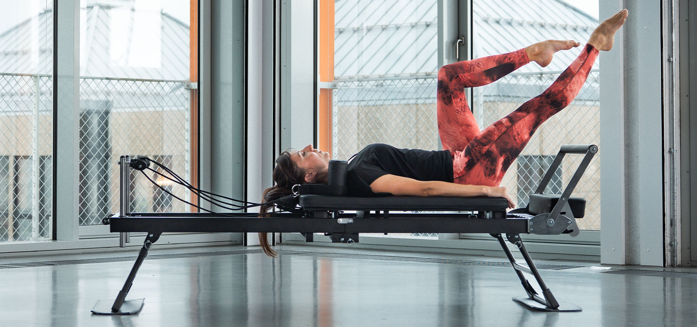 Femme faisant du Pilates sur un appareil reformer, avec des accessoires de fitness à proximité.