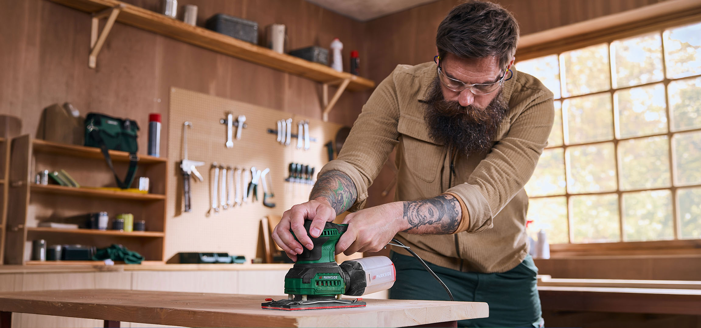 aiLabeling.aiLabelForImageAltText: Homme avec ponceuse électrique ponçant une table en bois dans un atelier.