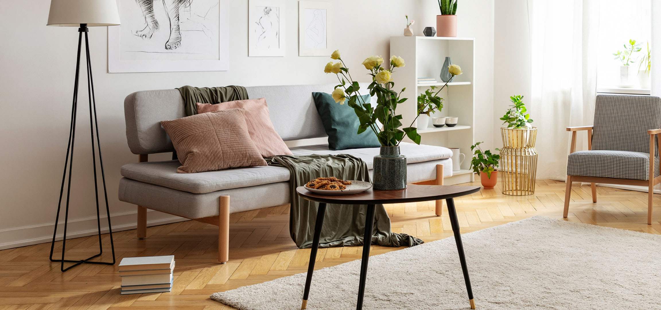 Salon confortable avec un canapé gris, des coussins, une table basse avec des biscuits et un vase de fleurs.