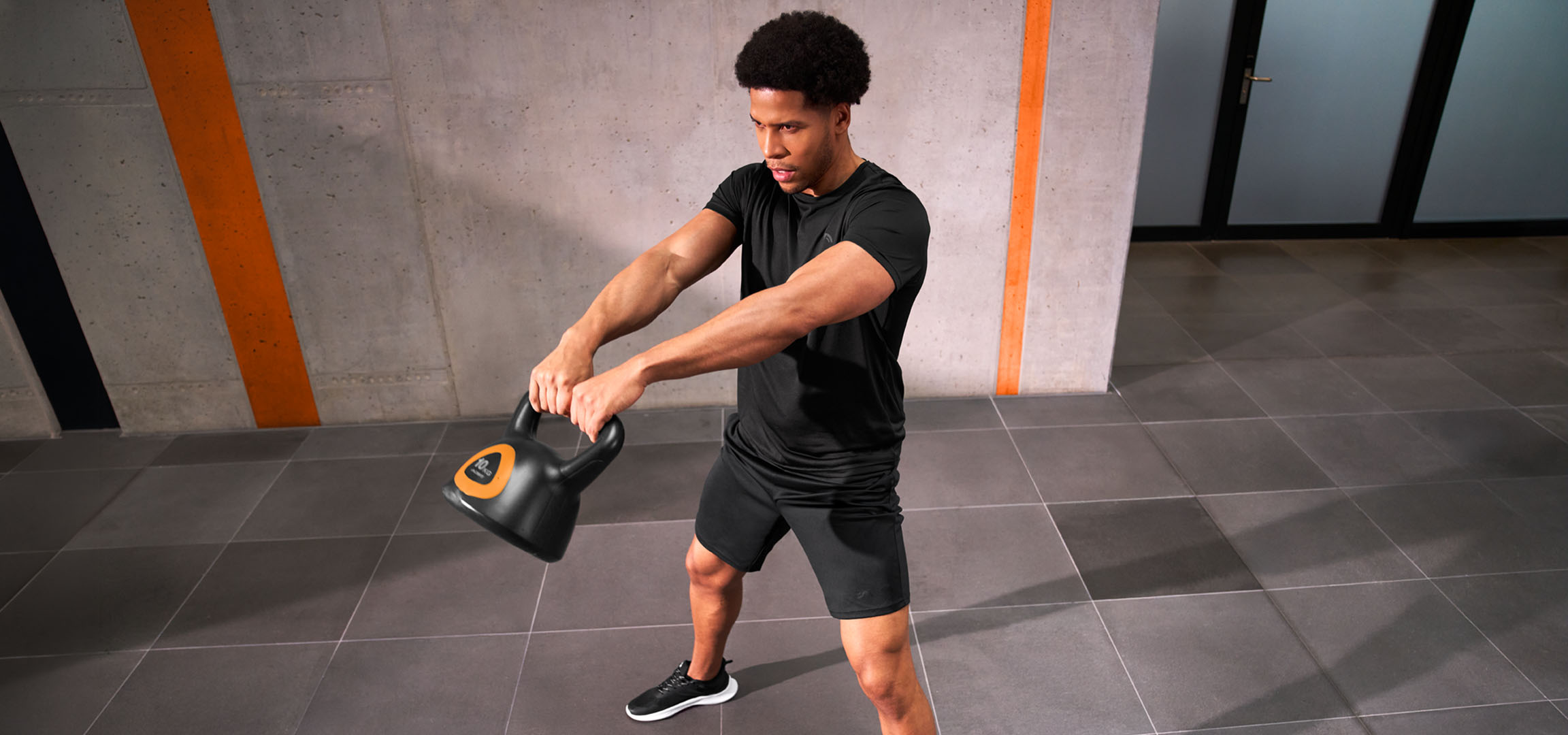 aiLabeling.aiLabelForImageAltText: Homme s'entraînant avec un kettlebell noir et orange.