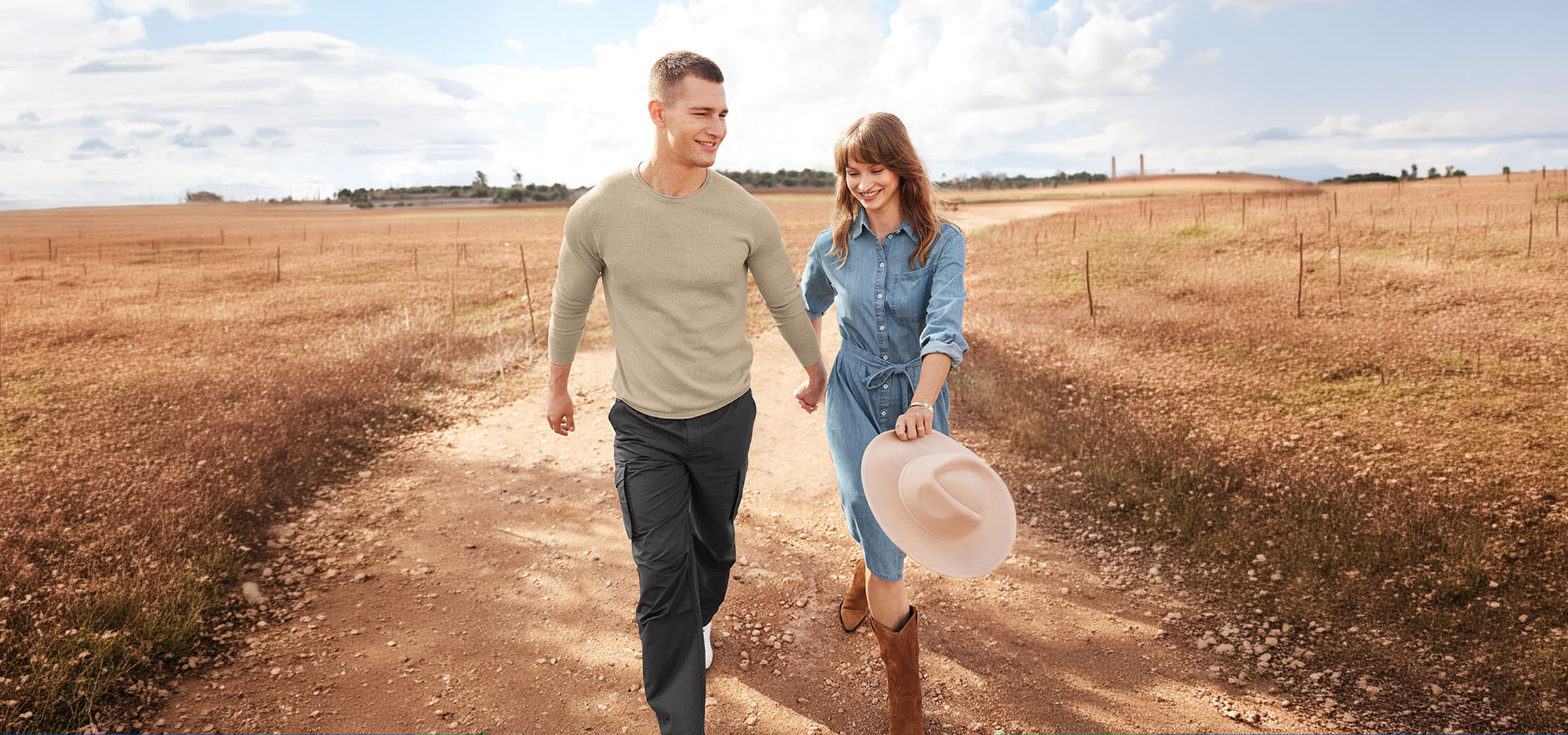 aiLabeling.aiLabelForImageAltText: Couple en tenue décontractée marchant sur un chemin de terre à travers un champ.