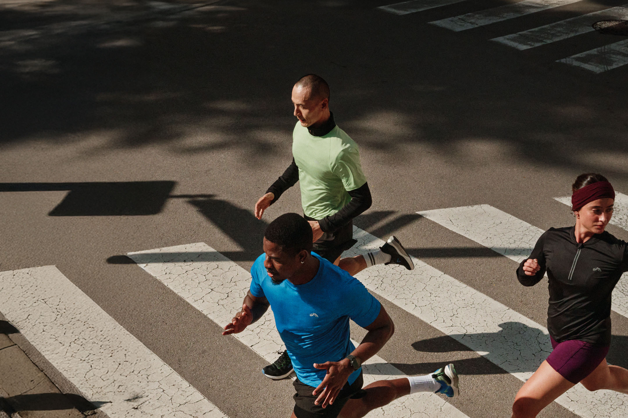 Trois coureurs en tenue de sport traversant un passage piéton en ville.