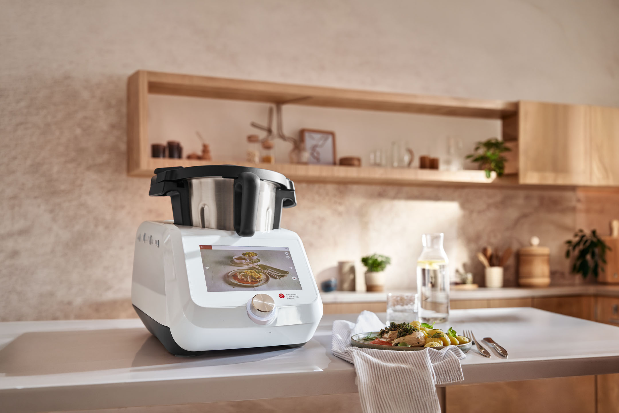 Appareil de cuisine intelligent sur un comptoir avec un repas préparé et une bouteille d'eau dans une cuisine moderne.