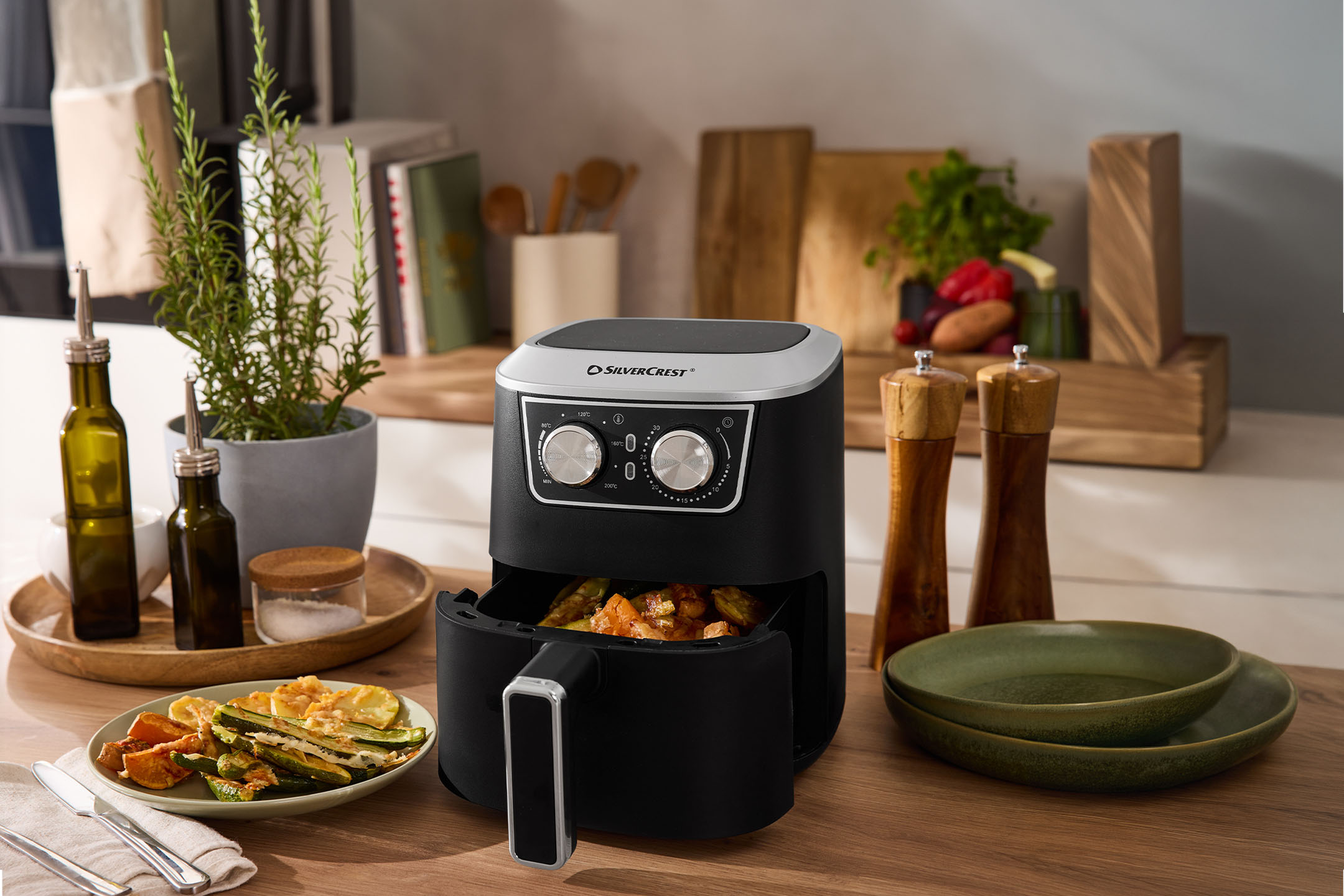 Friteuse à air noire avec légumes rôtis, herbes et épices dans une cuisine.
