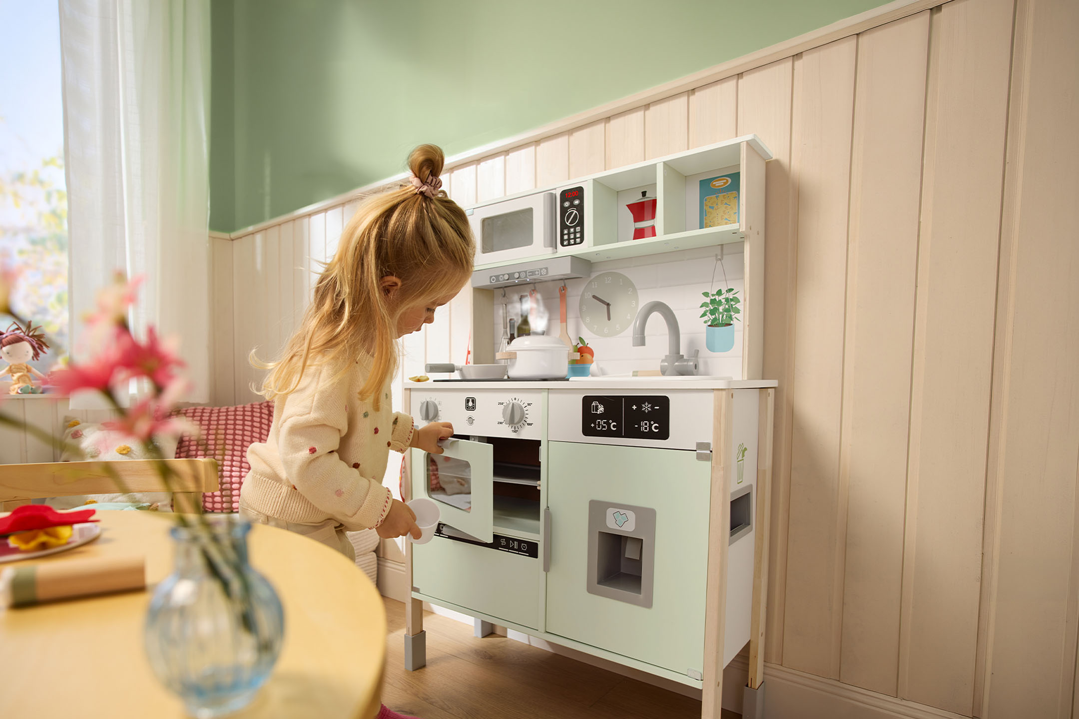 Petite fille jouant avec une cuisine jouet en bois, ouvrant la porte du four.