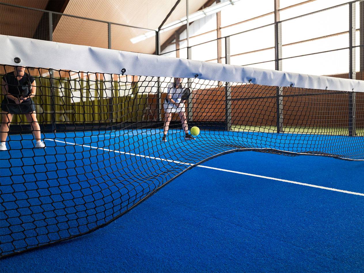 Deux femmes jouent au padel sur un court bleu, avec le filet au premier plan.