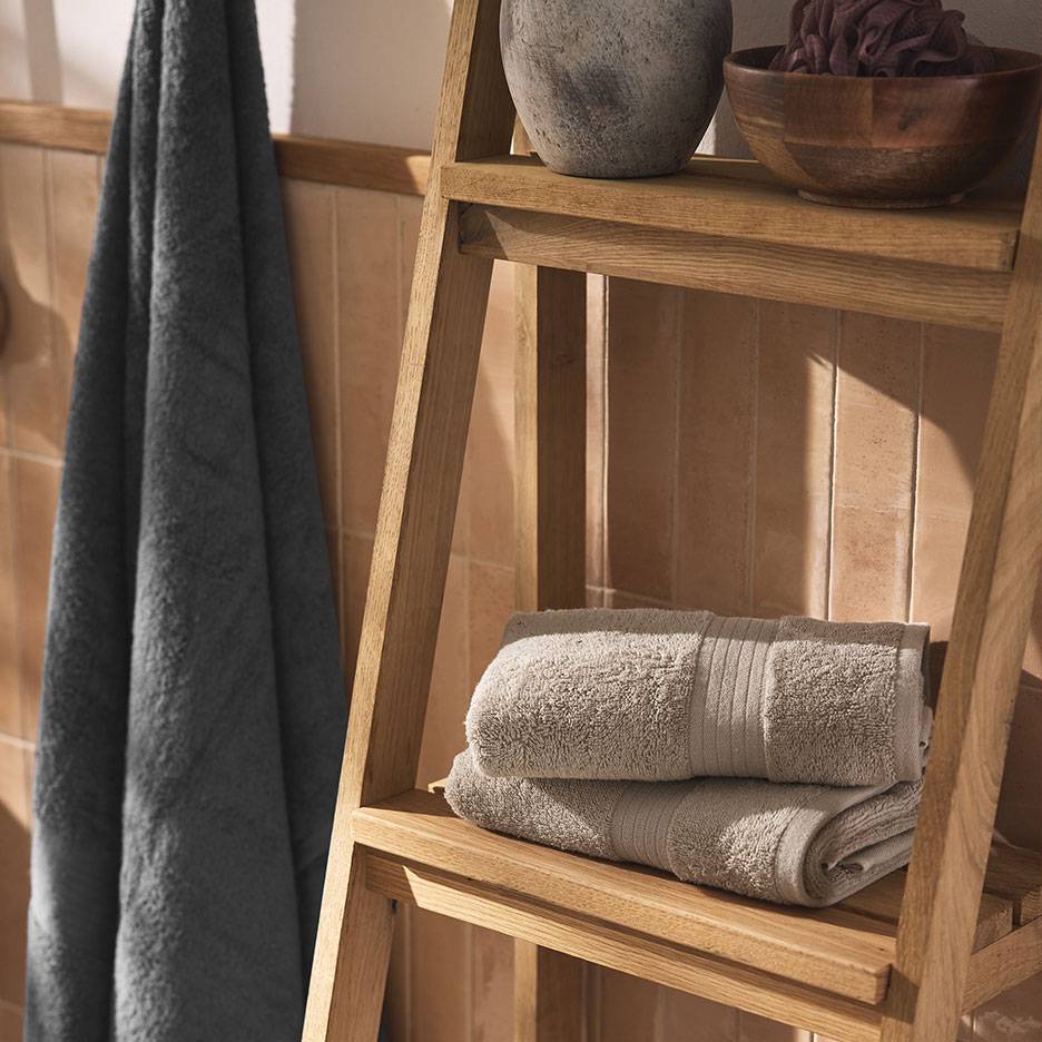 Serviettes grises sur une étagère en bois et une échelle dans une salle de bain carrelée.