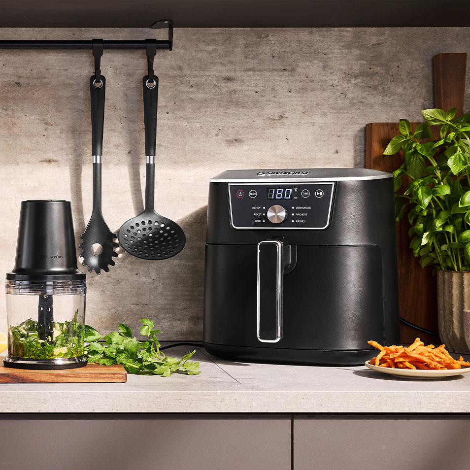 Friteuse à air et hachoir SilverCrest sur un comptoir de cuisine avec des herbes fraîches et des frites de patate douce.