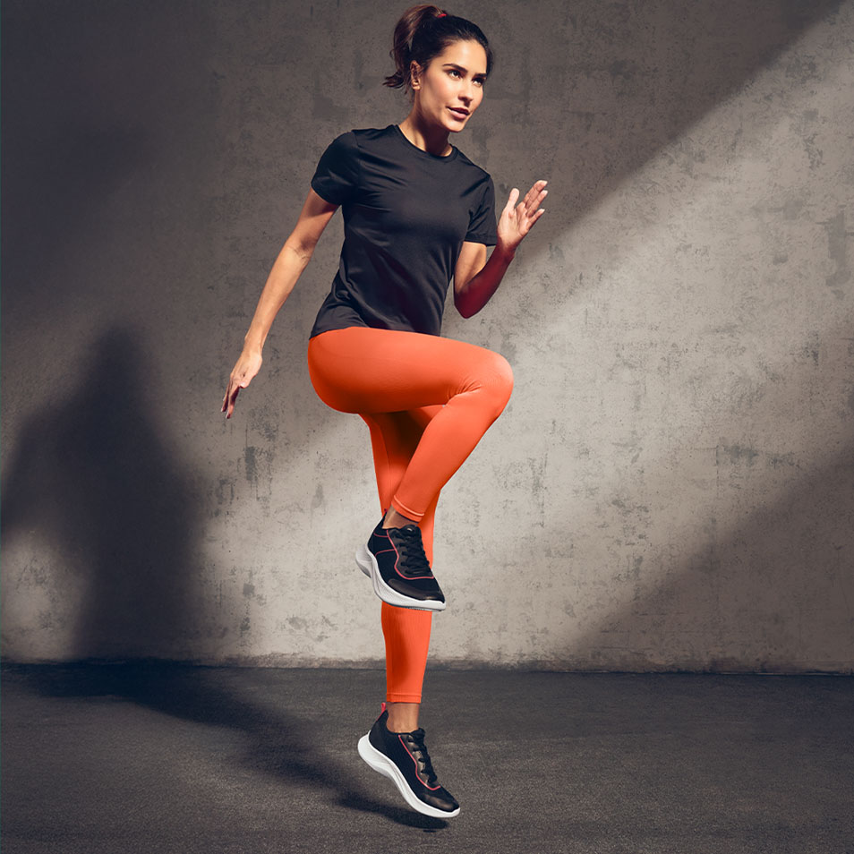 Femme en t-shirt noir et leggings orange faisant de l'exercice en salle.