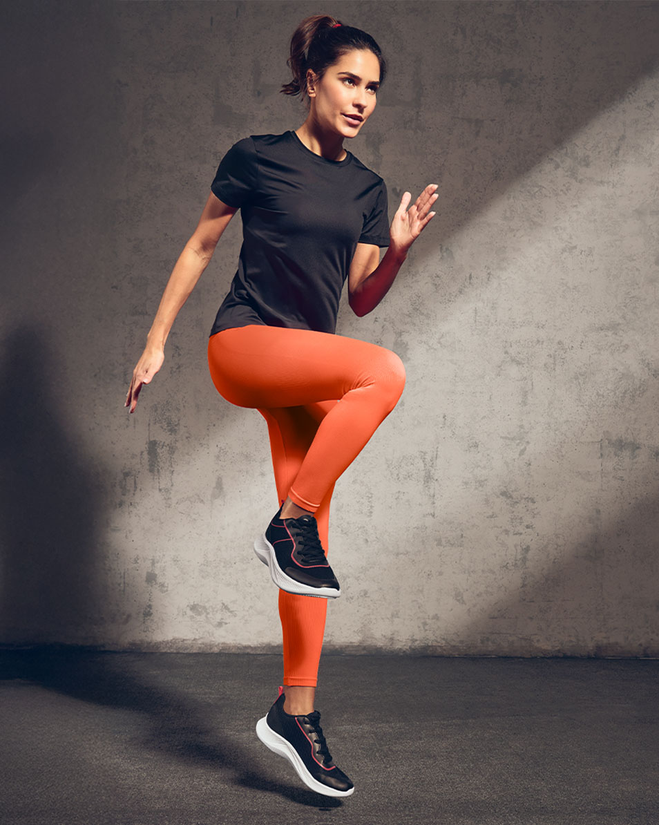 Femme en t-shirt de sport noir et legging orange faisant de l'exercice