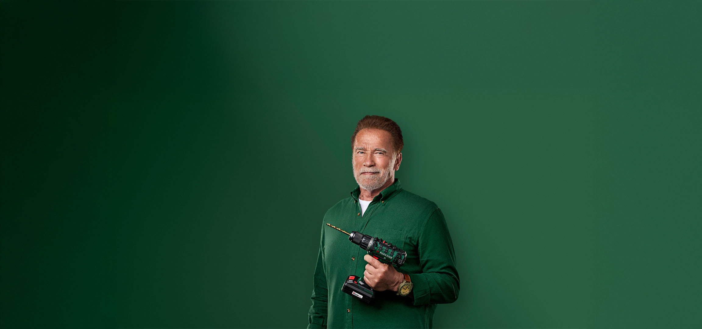 Arnold Schwarzenegger tenant une perceuse Parkside sur fond vert.