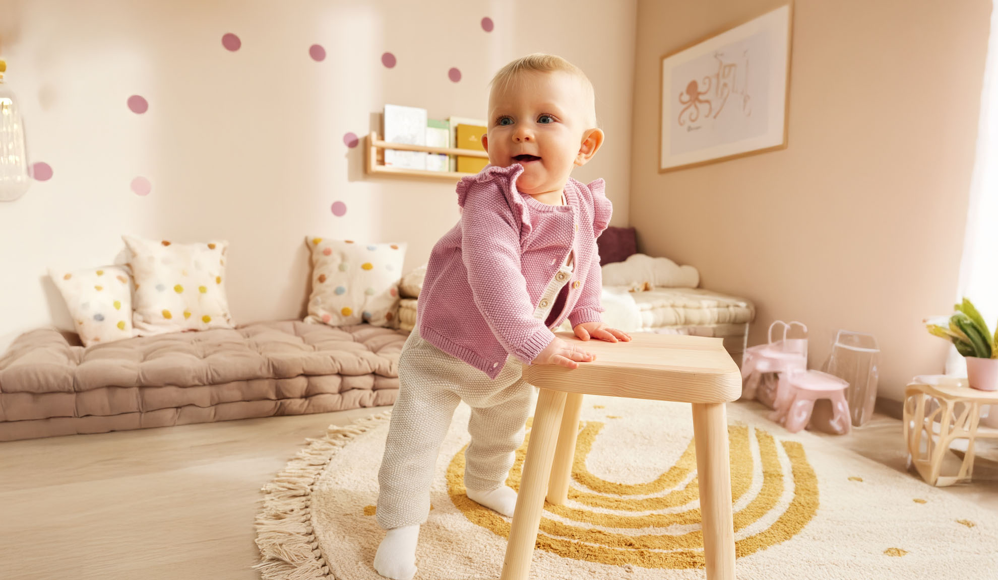 Un jeune enfant debout près d'un tabouret en bois dans une chambre d'enfant décorée de façon minimaliste.