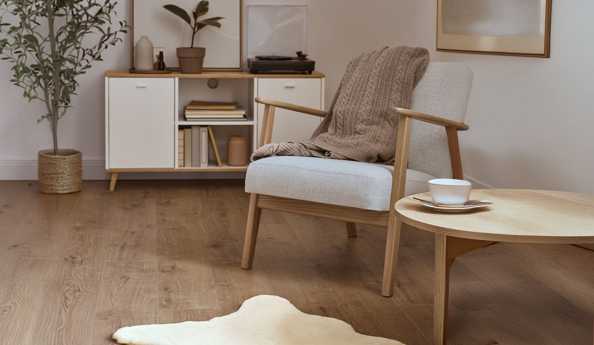 Fauteuil confortable avec plaid, table basse en bois et meuble de rangement dans un salon lumineux.