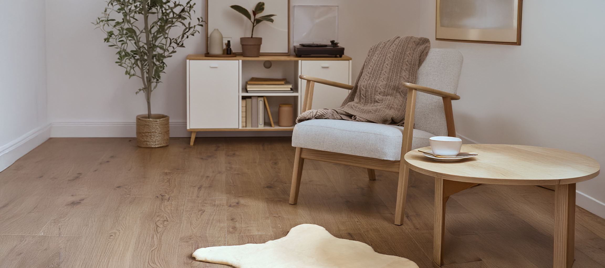 Fauteuil en tissu gris avec plaid tricoté, table basse en bois et buffet moderne.