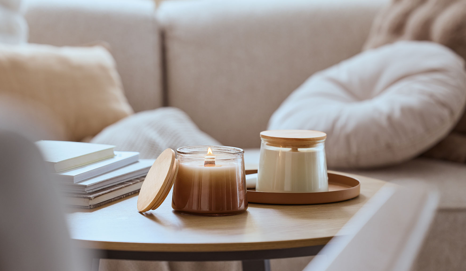 Deux bougies parfumées sur une table en bois, l'une allumée, avec un canapé confortable en arrière-plan.