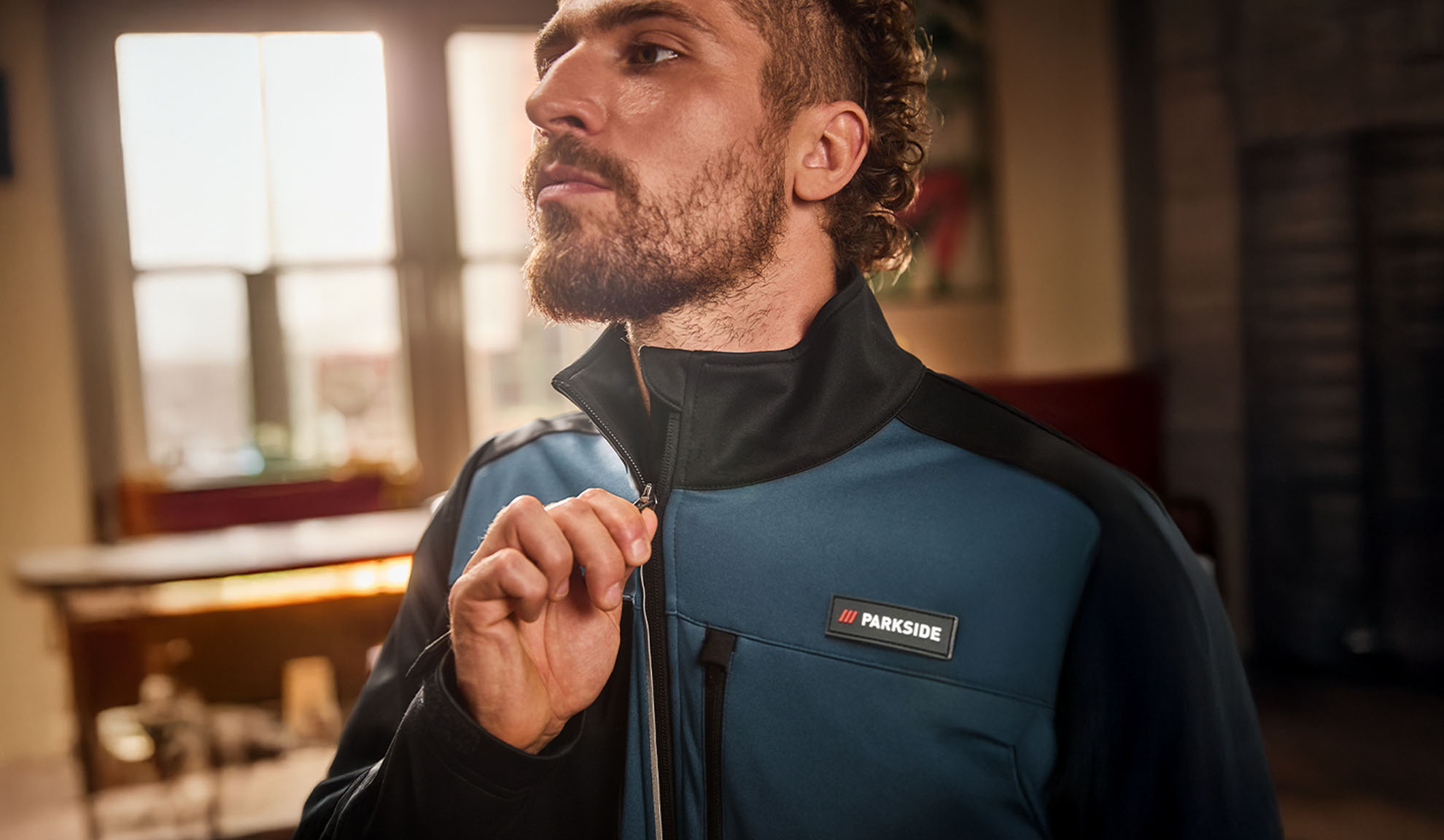 Homme en veste de travail Parkside bleue et noire, la fermant.