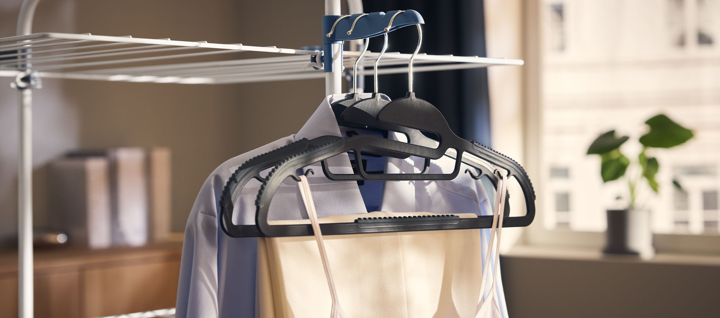 Vêtements sur cintres sur un étendoir, avec une plante en arrière-plan.