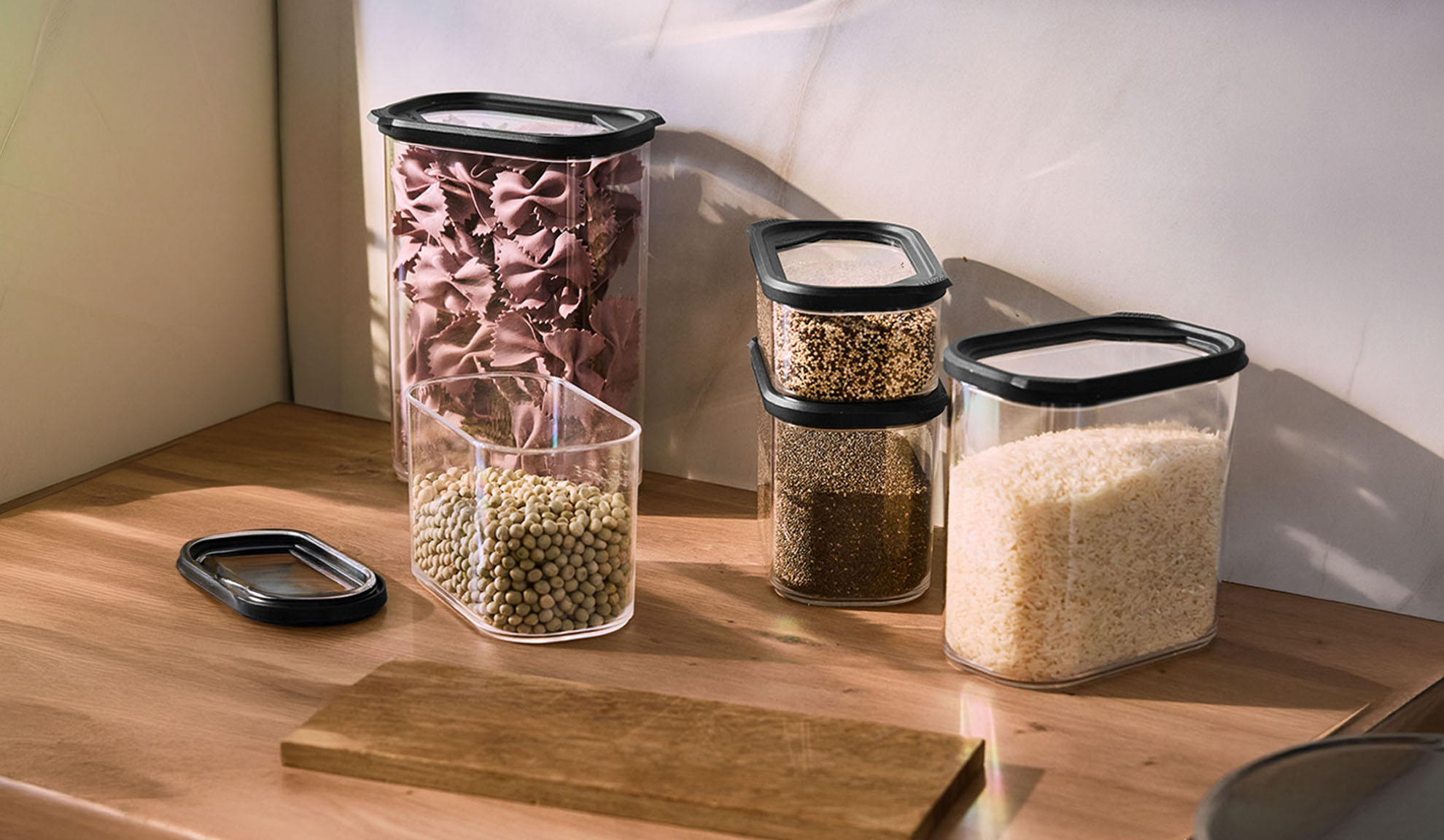 Récipients de rangement de cuisine transparents avec pâtes, lentilles, graines et riz sur un comptoir en bois.